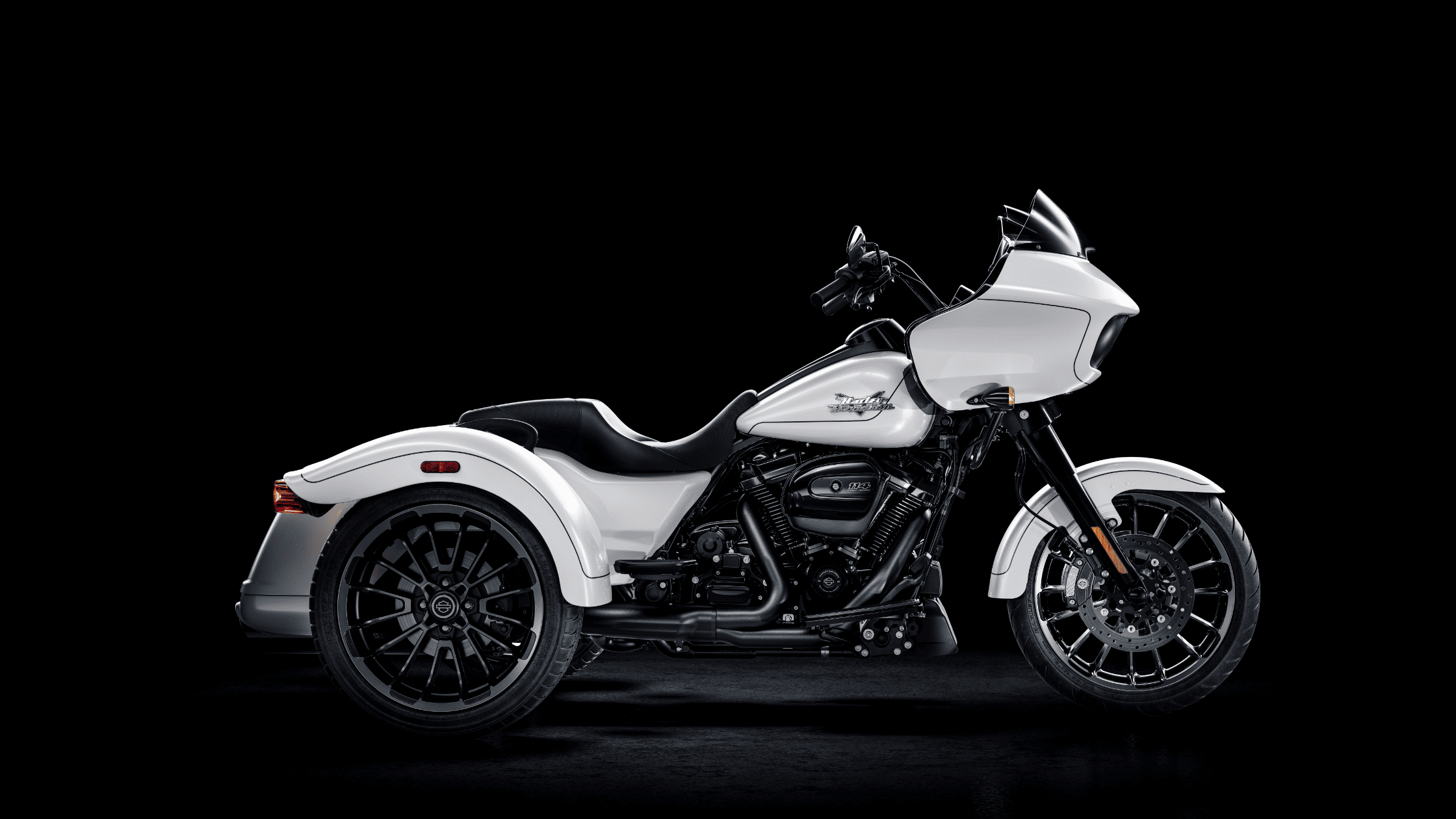 A white Harley-Davidson trike with a sleek fairing, black accents, and two rear wheels, set against a black background.